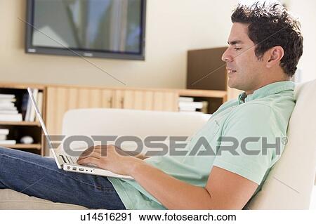 Stock Image - Man in living room using laptop. Fotosearch