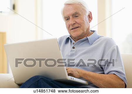 Stock Photo - Man in living room with laptop smiling. Fotosearch