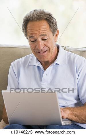 Stock Image - Man in living room with laptop. Fotosearch