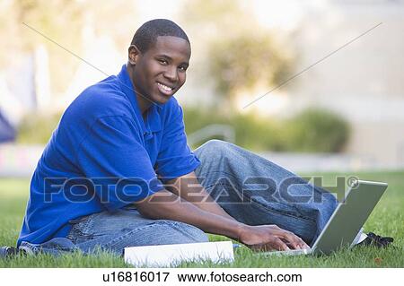 Stock Photo - Man outdoors sitting on grass with laptop (selective focus). Fotosearch