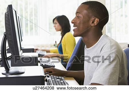 Stock Photo - Man sitting at a computer terminal with woman in background (selective focus/high key). Fotosearch