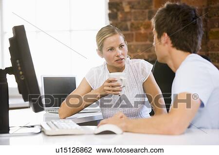 Stock Image - Two businesspeople in office drinking coffee and talking. Fotosearch