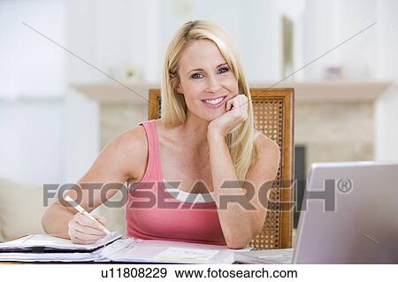 Stock Photo - Woman in dining room with laptop smiling. Fotosearch