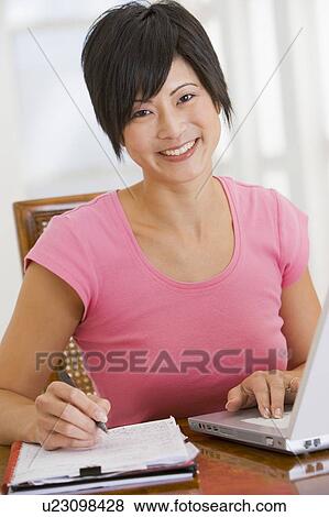Stock Photo - Woman in dining room with laptop smiling. Fotosearch