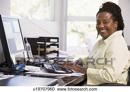 Stock Image - Woman in home office using computer and smiling. Fotosearch