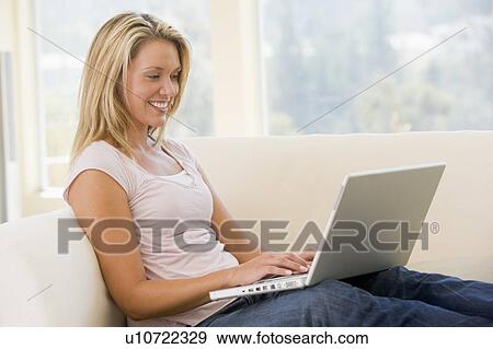 Stock Photo - Woman in living room using laptop smiling. Fotosearch