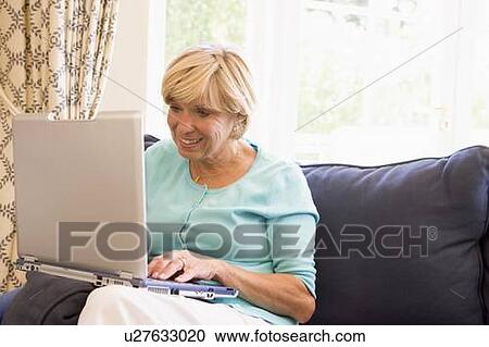 Stock Image - Woman in living room with laptop smiling. Fotosearch
