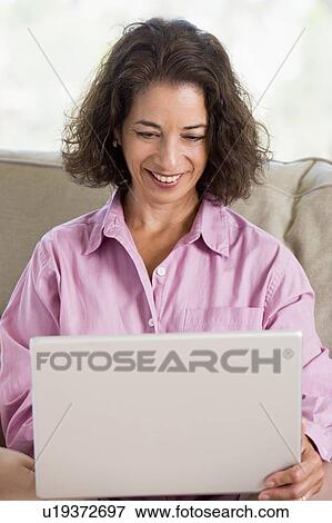 Stock Photo - Woman in living room with laptop smiling. Fotosearch