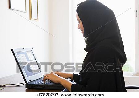 Stock Photo - Woman in office with laptop smiling (high key/selective focus). Fotosearch