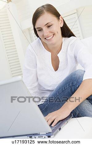 Stock Photography - Woman on patio using laptop and smiling. Fotosearch