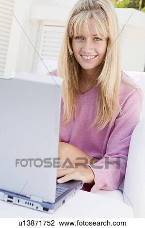 Stock Image - Woman on patio using laptop smiling. Fotosearch