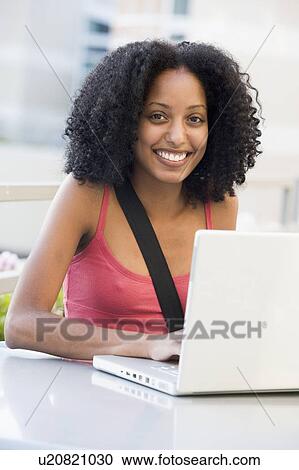 Woman sitting at table outdoors with laptop smiling (high key) View Large Photo Image Stock Image - Woman sitting at table outdoors with laptop smiling (high key). Fotosearch