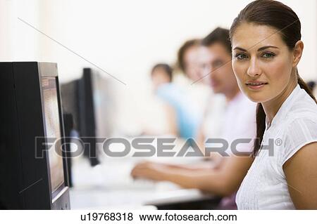 Stock Photo - Woman sitting in computer room with people in background. Fotosearch