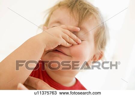 Stock Image - Baby indoors putting hand over face. Fotosearch