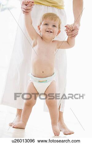 Mother helping baby walk indoors smiling View Large Photo Image Stock Photograph - Mother helping baby walk indoors smiling. Fotosearch
