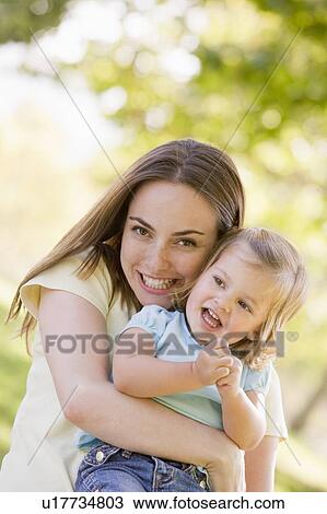 Stock Image - Mother holding daughter outdoors smiling. Fotosearch