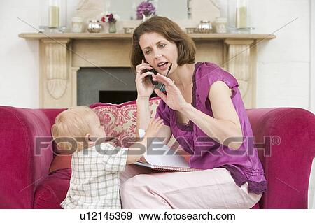 Stock Photo - Mother using telephone in living room with baby frowning. Fotosearch