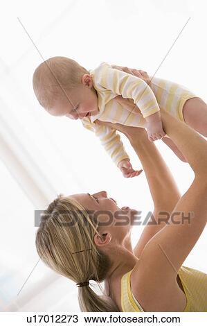 Mother holding baby indoors smiling View Large Photo Image Stock Image - Mother holding baby indoors smiling. Fotosearch