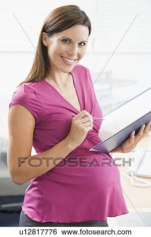 Pregnant woman at work writing in binder smiling View Large Photo Image Stock Photograph - Pregnant woman at work writing in binder smiling. Fotosearch