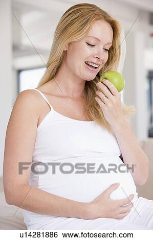 Stock Photograph - Pregnant woman eating apple and smiling. Fotosearch