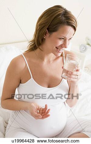 Pregnant woman in bedroom holding medicine and water smiling View Large Photo Image Stock Photo - Pregnant woman in bedroom holding medicine and water smiling. Fotosearch