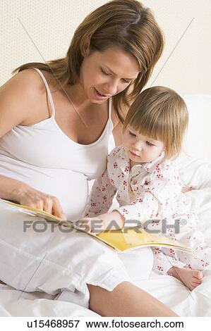Stock Photo - Pregnant woman in bedroom reading book with daughter. Fotosearch
