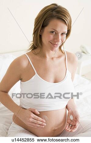 Pregnant woman in bedroom rubbing cream on belly smiling View Large Photo Image Stock Photography - Pregnant woman in bedroom rubbing cream on belly smiling. Fotosearch