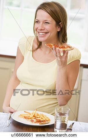 Pregnant woman in kitchen eating French fries and pizza smiling View Large Photo Image Stock Image - Pregnant woman in kitchen eating French fries and pizza smiling. Fotosearch