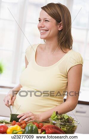Stock Photo - Pregnant woman in kitchen making a salad smiling. Fotosearch