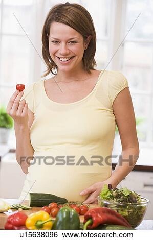 Stock Photograph - Pregnant woman in kitchen making a salad smiling. Fotosearch