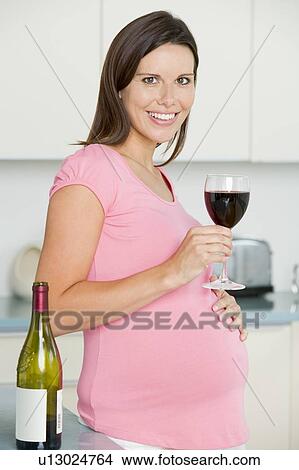 Pregnant woman in kitchen with glass of red wine smiling View Large Photo Image Picture - Pregnant woman in kitchen with glass of red wine smiling. Fotosearch