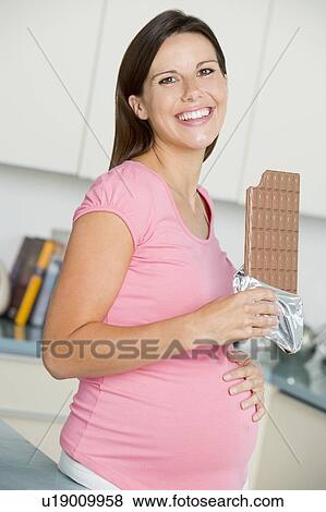 Pregnant woman in kitchen with large chocolate bar smiling View Large Photo Image Stock Photo - Pregnant woman in kitchen with large chocolate bar smiling. Fotosearch