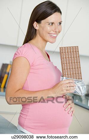 Stock Photo - Pregnant woman in kitchen with large chocolate bar smiling. Fotosearch