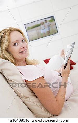 Pregnant woman reading magazine with television in background smiling View Large Photo Image Stock Photograph - Pregnant woman reading magazine with television in background smiling. Fotosearch