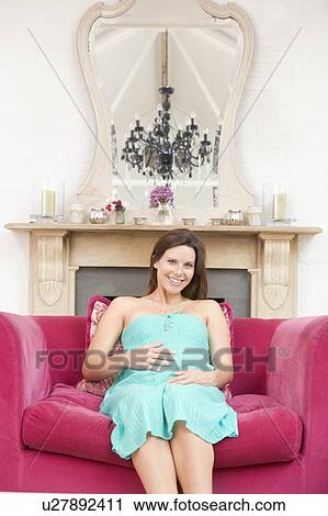 Stock Image - Pregnant woman sitting in living room smiling. Fotosearch