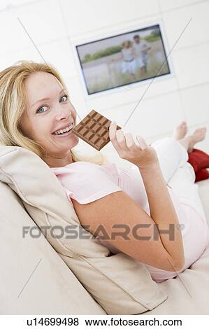 Stock Photo - Pregnant woman watching television and eating chocolate smiling. Fotosearch