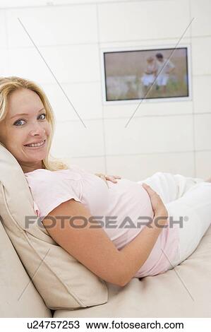 Stock Image - Pregnant woman watching television smiling. Fotosearch