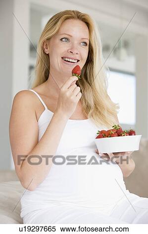 Stock Photography - Pregnant woman with bowl of strawberries smiling. Fotosearch