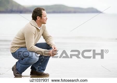 Stock Image - Man crouching on beach. Fotosearch