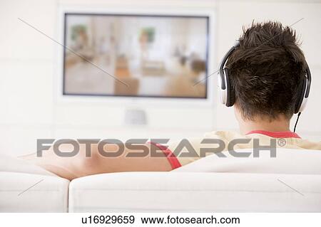 Stock Photo - Man in living room watching television and wearing headphones. Fotosearch