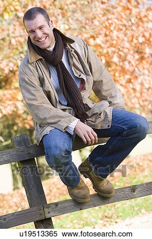 Man outdoors at park sitting on fence smiling (selective focus) View Large Photo Image Stock Photography - Man outdoors at park sitting on fence smiling (selective focus). Fotosearch