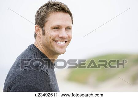 Stock Image - Man standing at beach smiling. Fotosearch