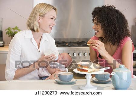 Mother and baby in kitchen with friend eating cake and smiling View Large Photo Image Stock Photo - Mother and baby in kitchen with friend eating cake and smiling. Fotosearch