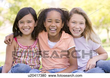 Three young girl friends sitting outdoors smiling View Large Photo Image Stock Image - Three young girl friends sitting outdoors smiling. Fotosearch