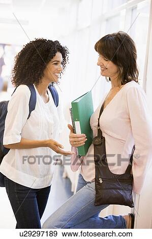 Two women in corridor with books talking (high key) View Large Photo Image Stock Photo - Two women in corridor with books talking (high key). Fotosearch