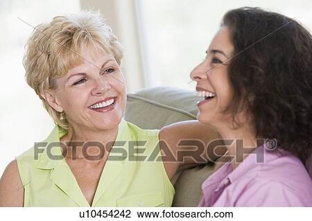 Stock Image - Two women in living room talking and smiling. Fotosearch
