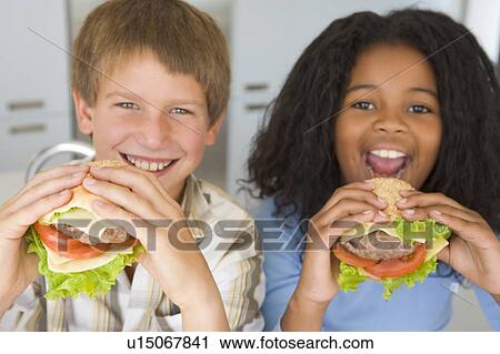 Two young children in kitchen eating cheeseburgers smiling View Large Photo Image Stock Image - Two young children in kitchen eating cheeseburgers smiling. Fotosearch