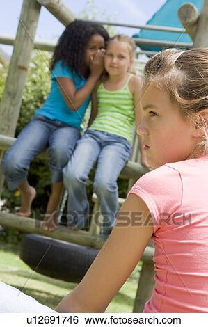 Stock Photograph - Two young girl friends at a playground whispering about other girl in foreground. Fotosearch