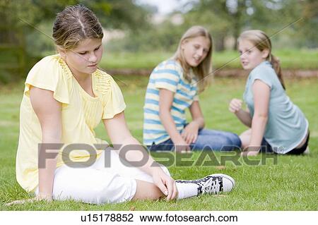 Stock Image - Two young girls bullying other young girl outdoors. Fotosearch