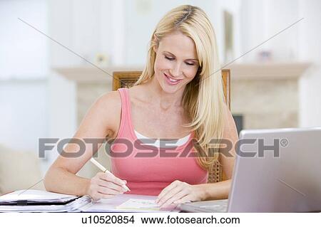 Picture - Woman in dining room with laptop smiling. Fotosearch